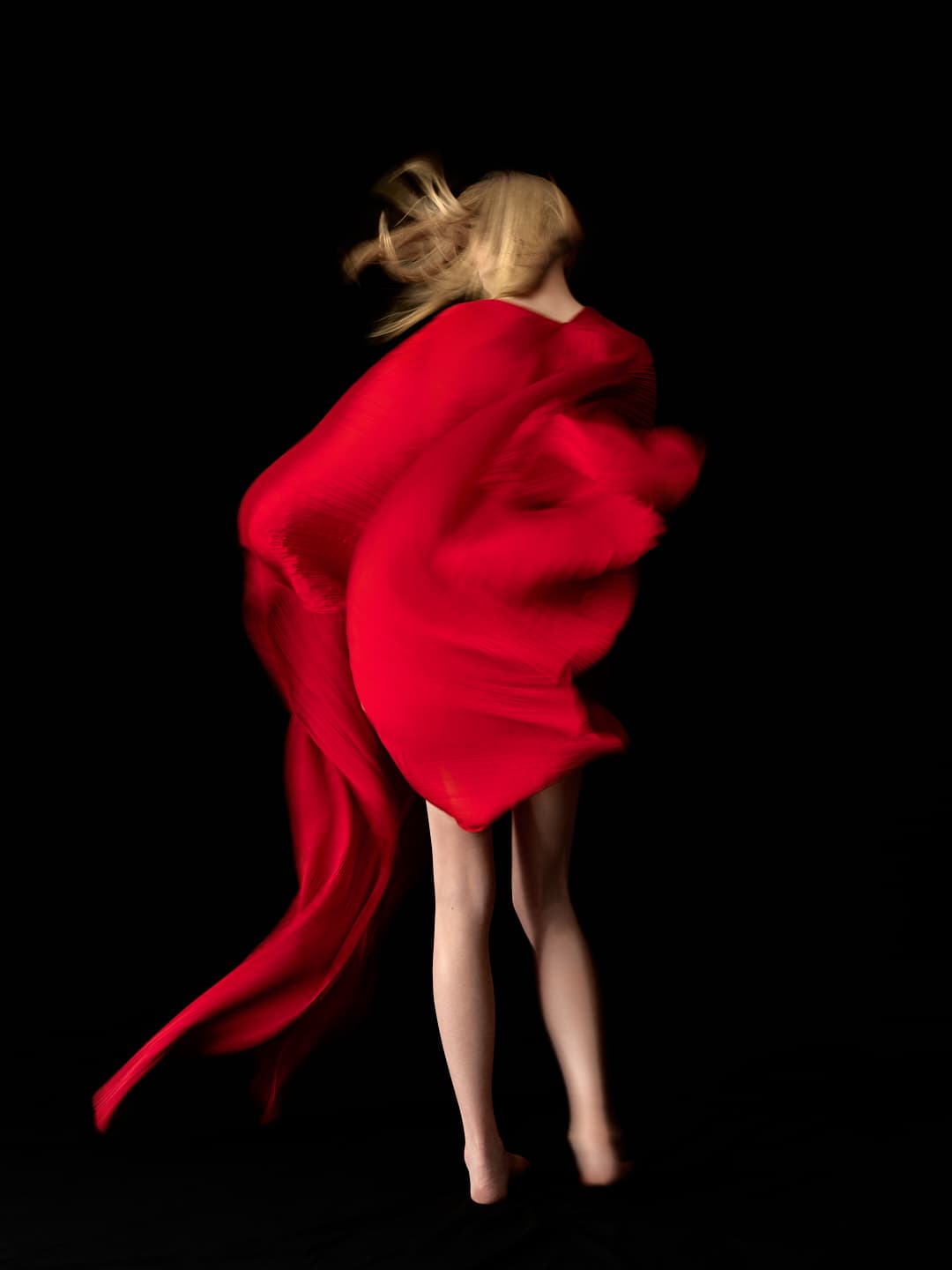 Silhouette en mouvement avec un tissu rouge flottant sur fond noir.