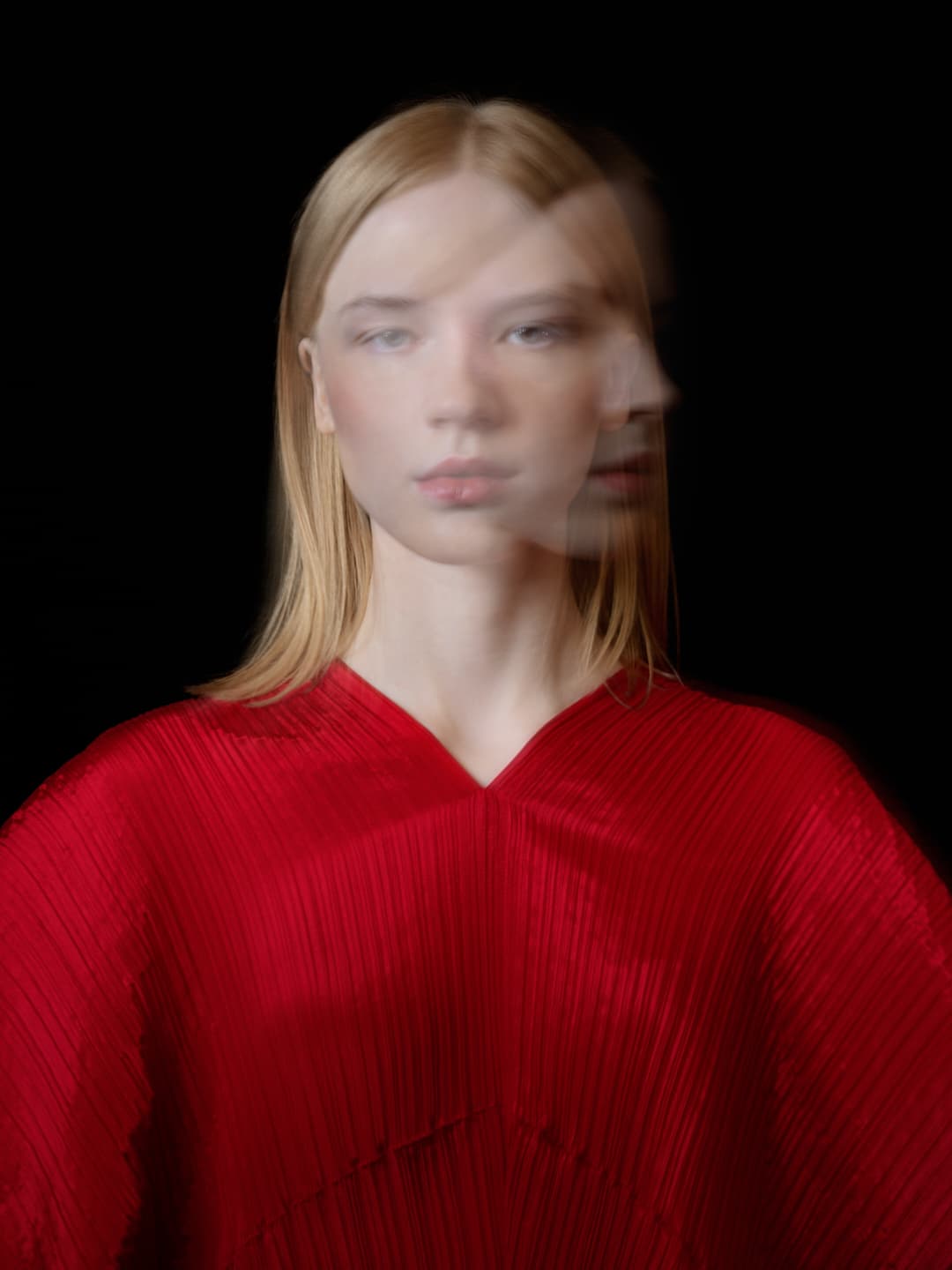 Portrait en double exposition d'une modèle portant une robe plissée rouge Issey Miyake.