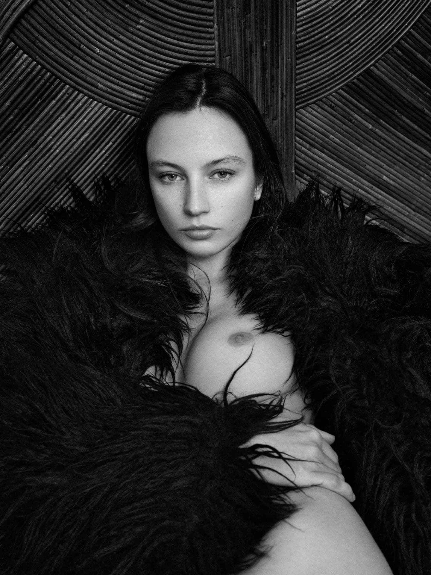 Frontal portrait wrapped in black fur against a fan-shaped rattan headboard.