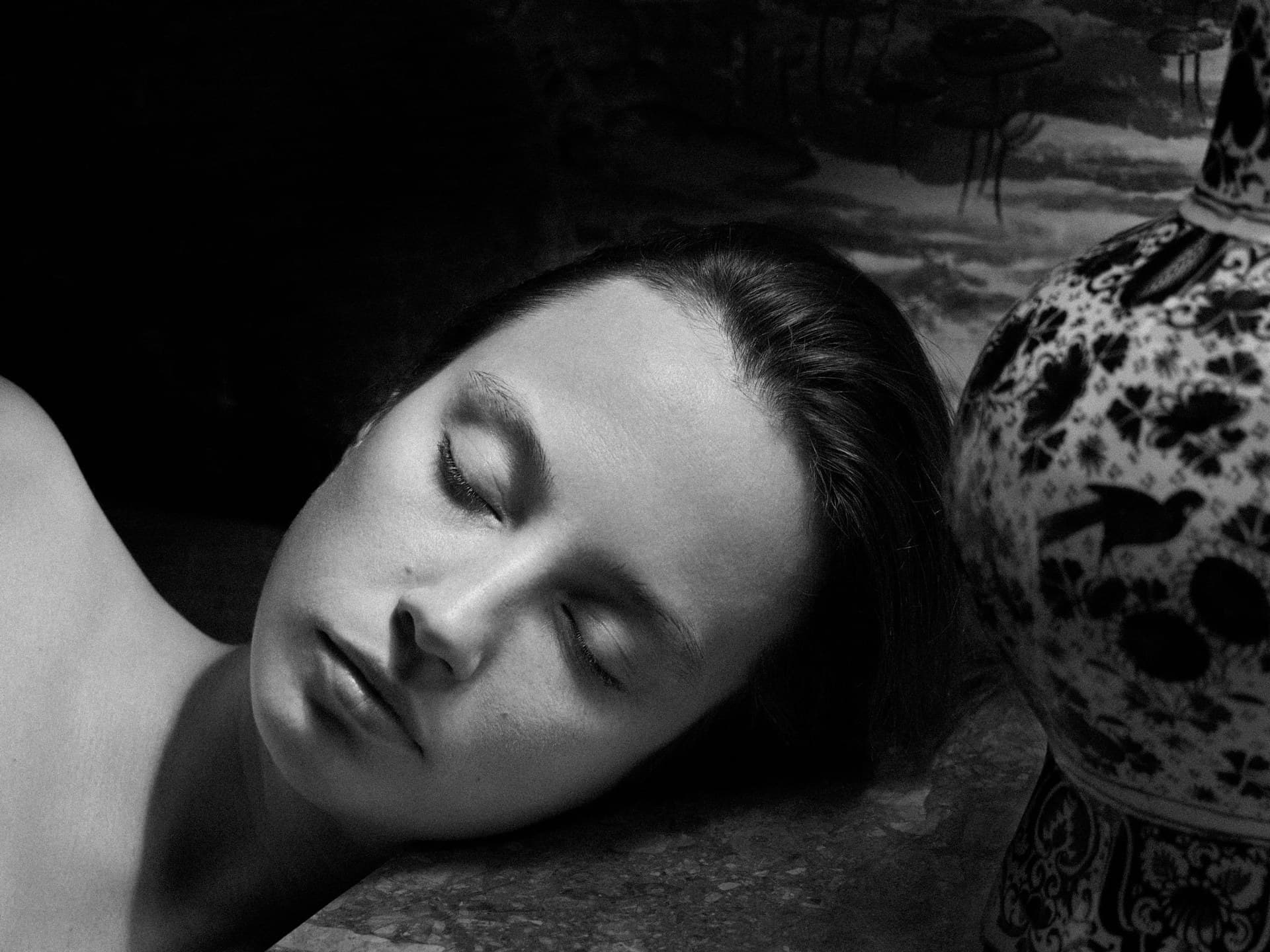 Face surrendered to sleep beside a Delft vase, in black and white chiaroscuro.