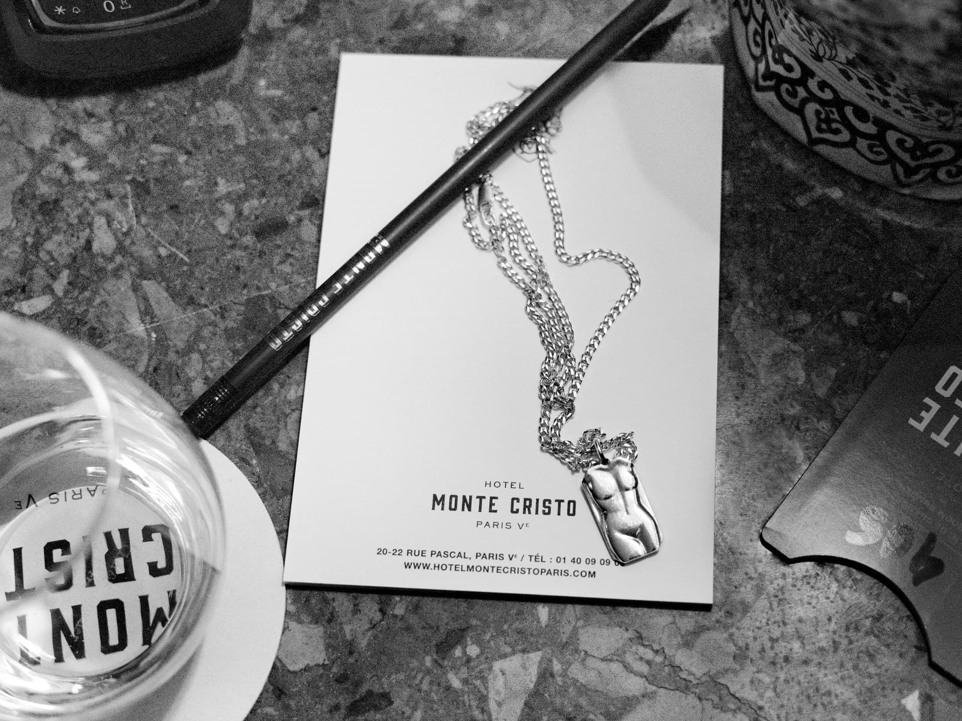 Still life with the hotel notepad: pencil, glass and a necklace bearing a female torso.